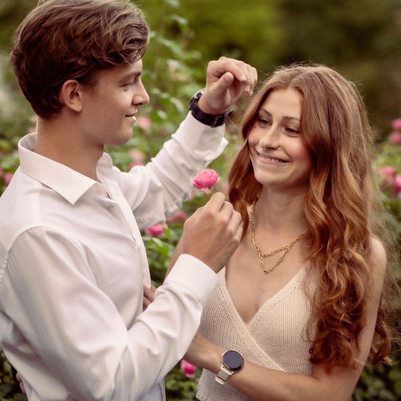 Casal sorridente em jardim, ele oferecendo uma flor a ela